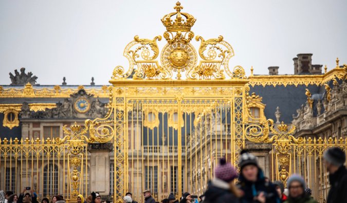 The ornate golden gates of the Palace of Versailles near Paris, France surrounded by tourists