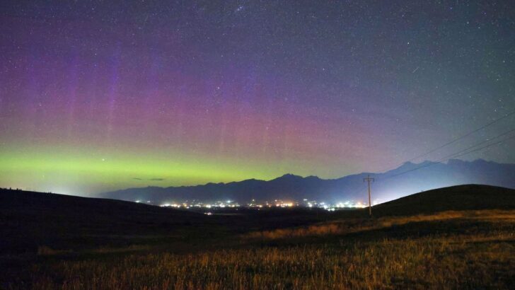 Auroras boreales sobre un paisaje nocturno con luces de ciudad y cielo estrellado