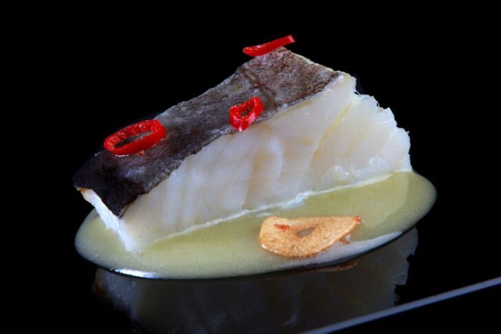 Plato de bacalao con ajo y guindilla sobre salsa en fondo negro