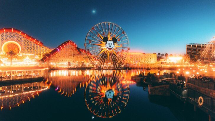 Noria iluminada con cara de Mickey Mouse en Disneyland reflejada en el agua durante la noche