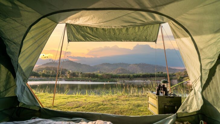 Vista desde una tienda de campaña hacia un lago al atardecer con montañas al fondo