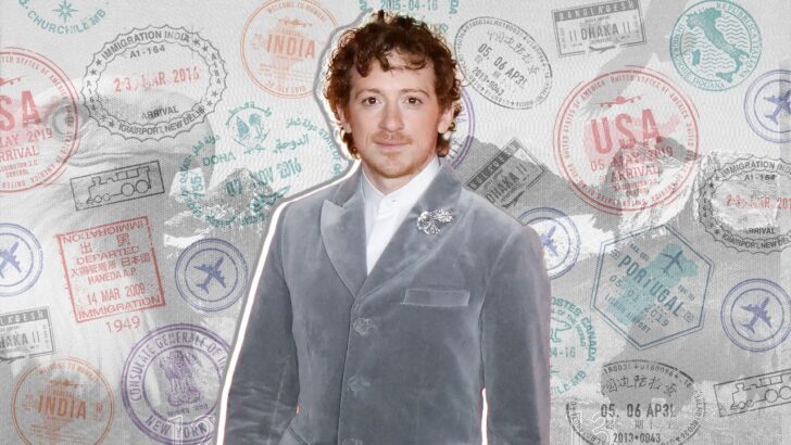 Ethan Slater con fondo de sellos de pasaporte, vestido formalmente