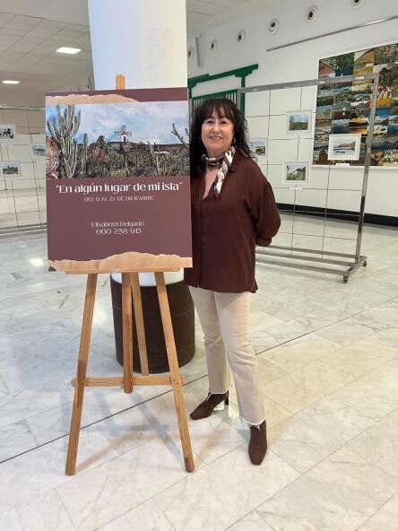 Artista junto a cartel de exposición en aeropuerto de Lanzarote