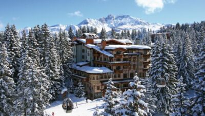Hotel rodeado de nieve y árboles en Courchevel con montañas al fondo