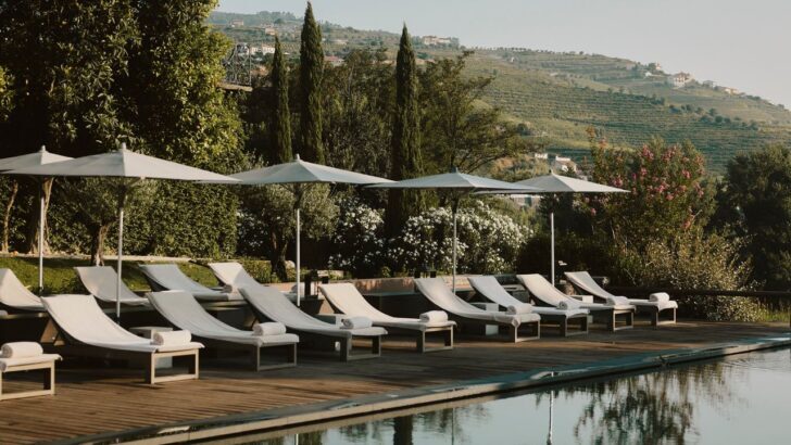 Piscina con tumbonas y sombrillas frente a montañas verdes