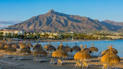 Playa con sombrillas de paja y montañas al fondo en Marbella, España