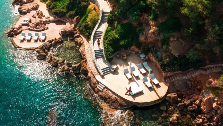 Vista aérea de un resort costero con terrazas y tumbonas junto al mar